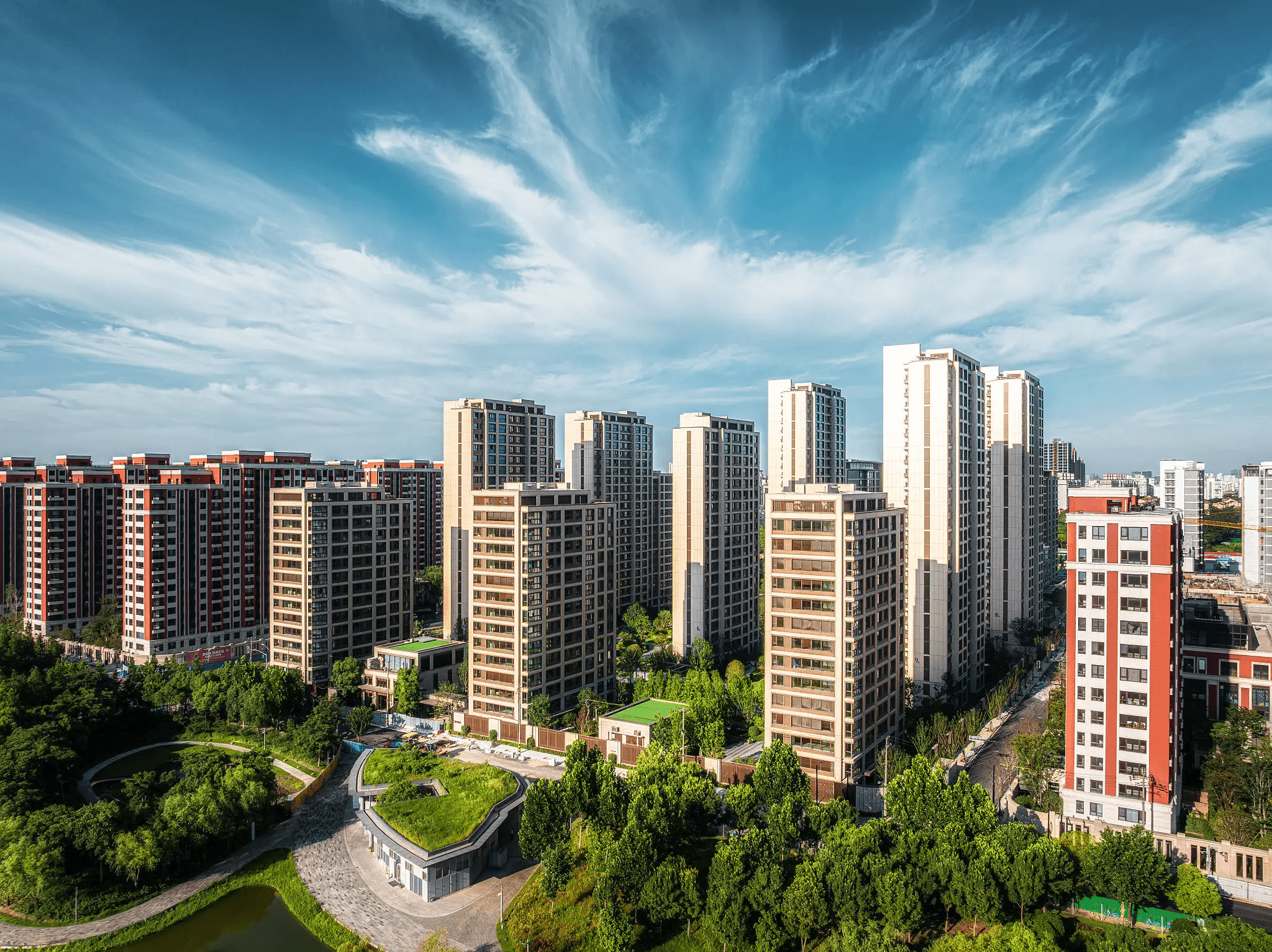 Modern high-rise residential buildings surrounded by greenery under a blue sky.